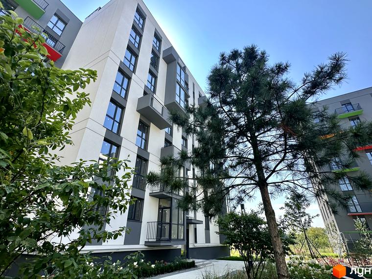 Житловий комплекс Проект Панорама з білими фасадами та темними вікнами, поруч зелені насадження та дерева, блакитне небо.