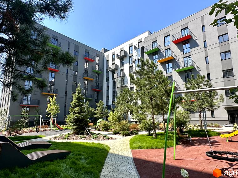 Житловий комплекс Проект Панорама з яскравими балконами та зеленою прибудинковою територією з дитячим майданчиком.