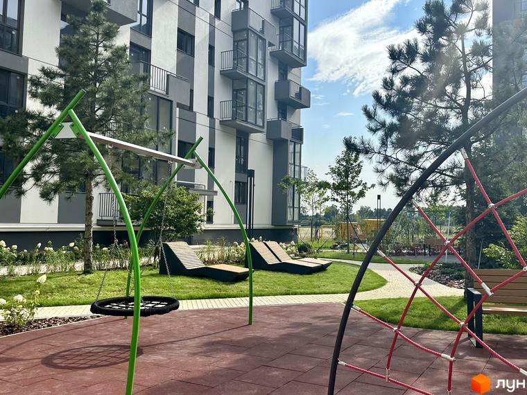 Житловий комплекс Проект Панорама: сучасна архітектура будинку та облаштований дитячий майданчик з гойдалками та пісочницею.