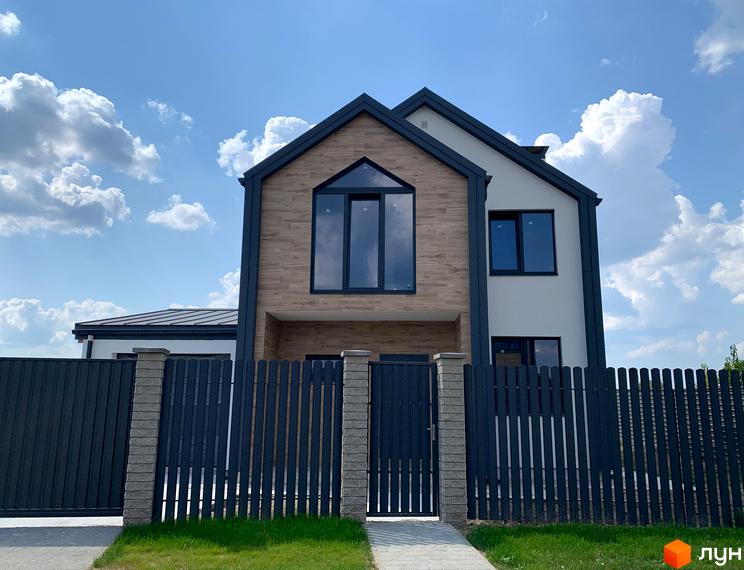 Котеджне містечко КМ Європа: двоповерховий будинок з великими вікнами та дерев'яним оздобленням фасаду, огороджений парканом.