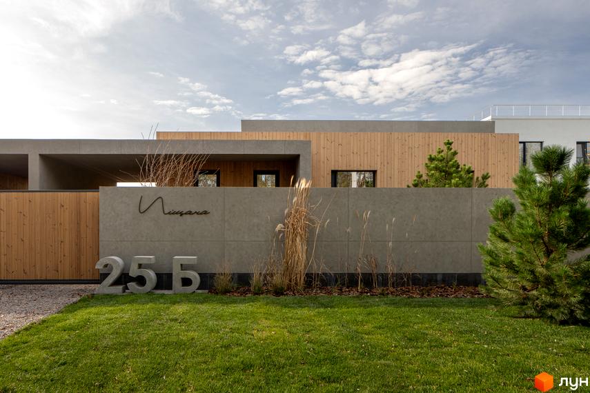 Фасад житлового комплексу на вул. Піщана, 25а, 25б, з сірою стіною, дерев'яними елементами та зеленим газоном.