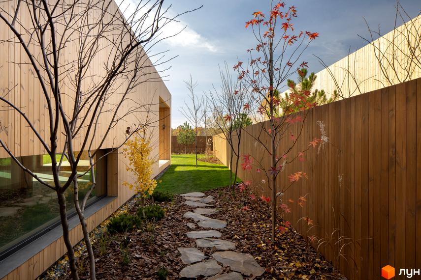 Будинок з дерев'яним фасадом та прибудинкова територія з кам'яною доріжкою та деревами з червоним листям. Житловий комплекс на вул. Піщана, 25а, 25б.