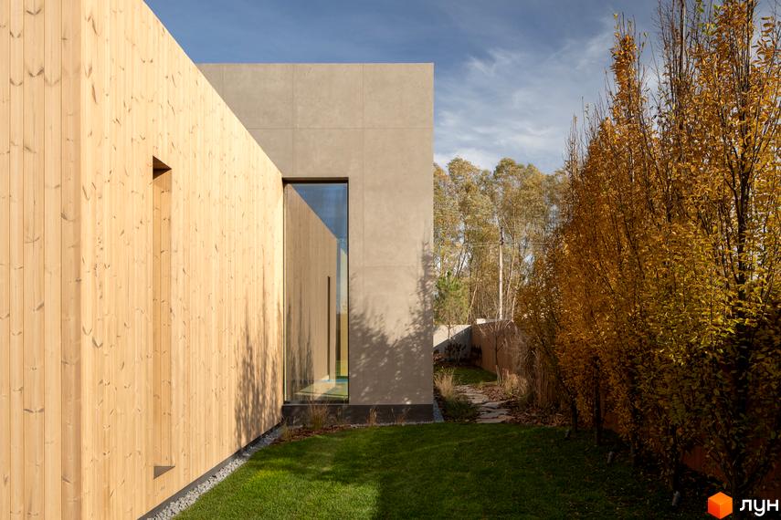 Зовнішній вигляд будинку з дерев'яною та кам'яною обробкою, зелений газон та дерева з жовтим листям. Вул. Піщана, 25а, 25б.