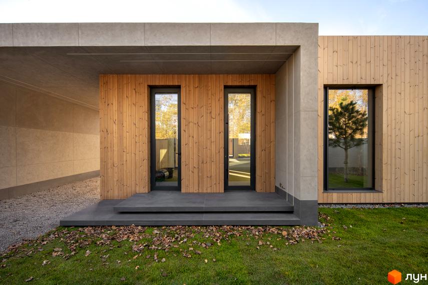 Зовнішній вигляд будинку з дерев'яною обшивкою та великими вікнами. Прибудинкова територія з газоном та опалим листям.