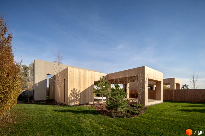 Двоповерховий будинок з дерев'яним фасадом та великими вікнами. На території зелена трава та дерева.