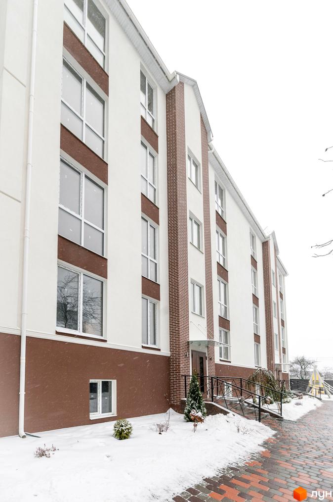 Житловий комплекс SMART IDEA. Зовнішній вигляд будівлі з біло-коричневим фасадом та цегляними вставками взимку. Прибудинкова територія вкрита снігом.