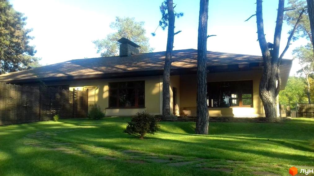 Будинок житлового комплексу КМ Шишкино з великими вікнами на зеленій території з газоном та деревами.