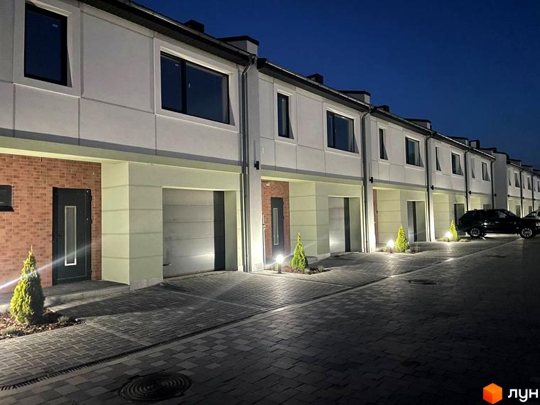 Таунхауси „Садовий Клуб“ зі світлими фасадами, великими вікнами та гаражами. Прибудинкова територія з бруківкою та освітленням.