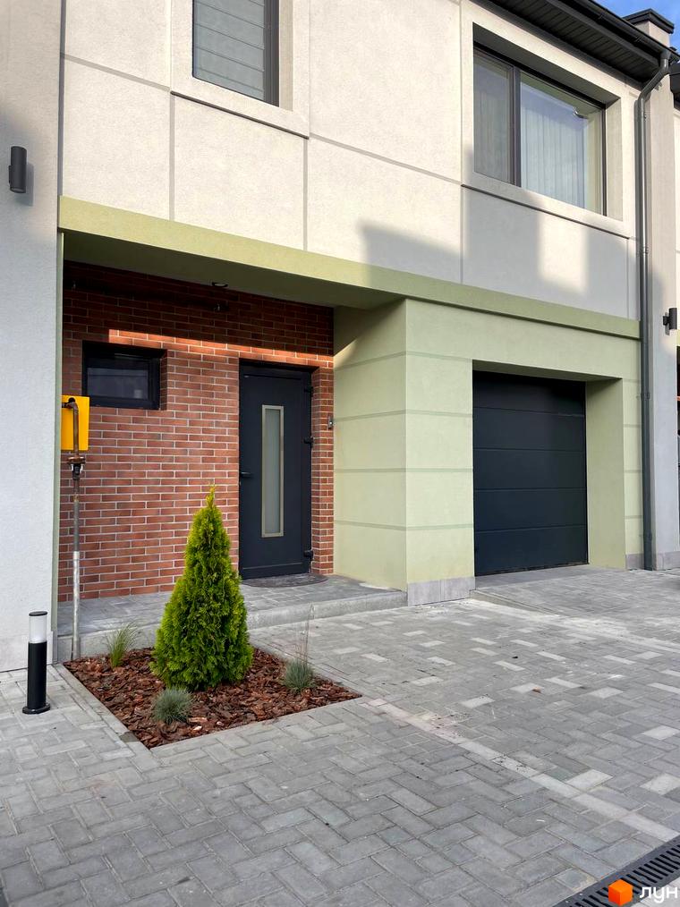 Таунхауси „Садовий Клуб“: двоповерхові будинки з цегляним фасадом та гаражем, перед якими розташована прибудинкова територія з туєю та бруківкою.