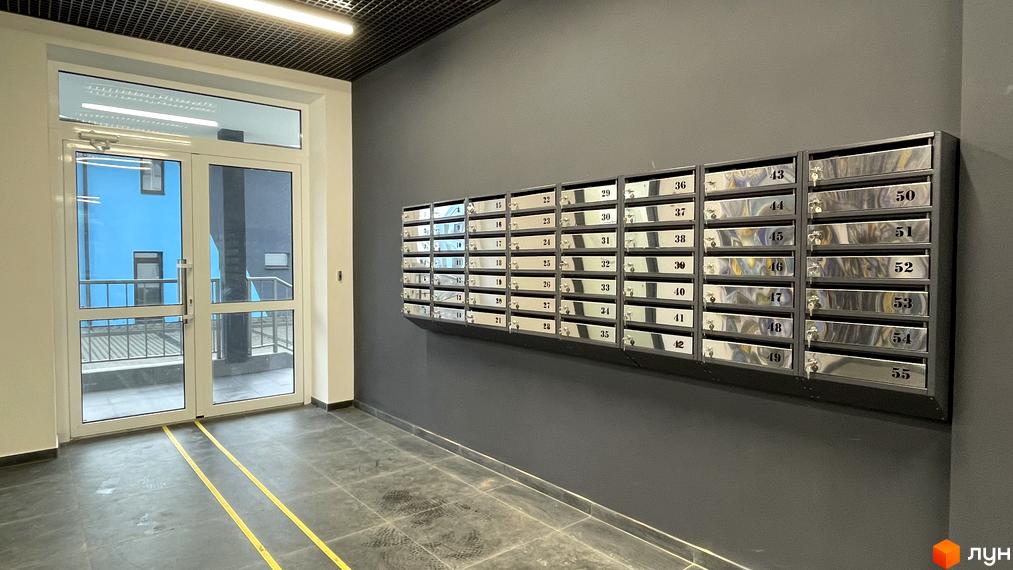 Частина Житлового комплексу One Family: вхідний хол з поштовими скриньками та прозорими дверима, що ведуть до синього фасаду будинку.