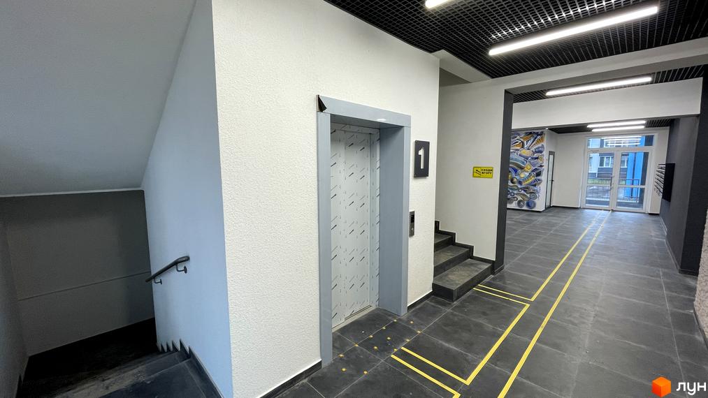 Вестибюль Житлового комплексу One Family з ліфтом, сходовою кліткою та вхідними дверима. На підлозі темна плитка з жовтою розміткою.