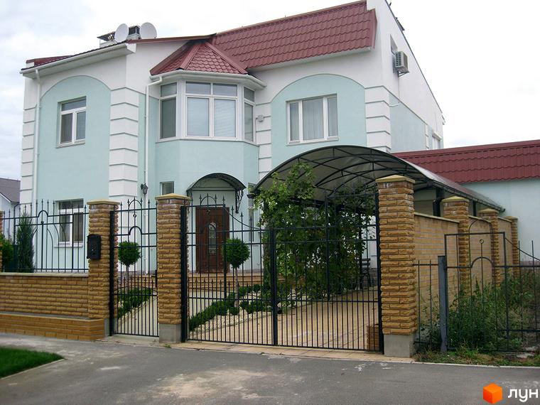 Зовнішній вигляд будинку КМ Нова Богданівка з блакитною фасадною обробкою та червоною покрівлею. Прибудинкова територія огороджена та озеленена.
