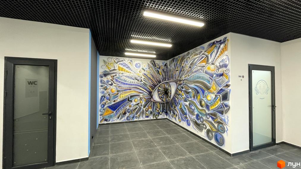 Інтер'єр приміщення з графіті на стіні у вигляді ока та елементів міста. Двері з табличкою WC та скляні двері з малюнком.