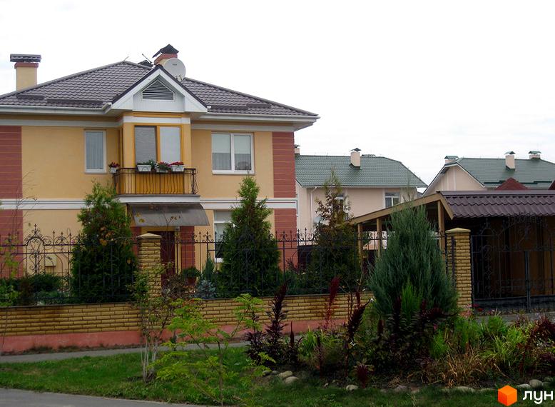 Зовнішній вигляд будинку в житловому комплексі КМ Нова Богданівка з квітами на балконі та доглянутою прибудинковою територією.