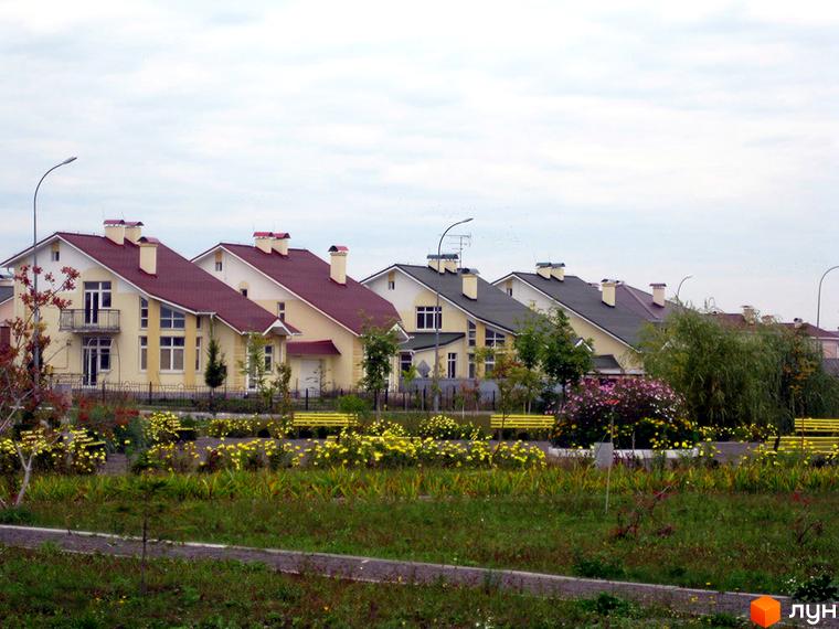 Котеджне містечко Нова Богданівка. Житлові будинки з червоними дахами та жовтими фасадами. На передньому плані газон з квітами та лавками.