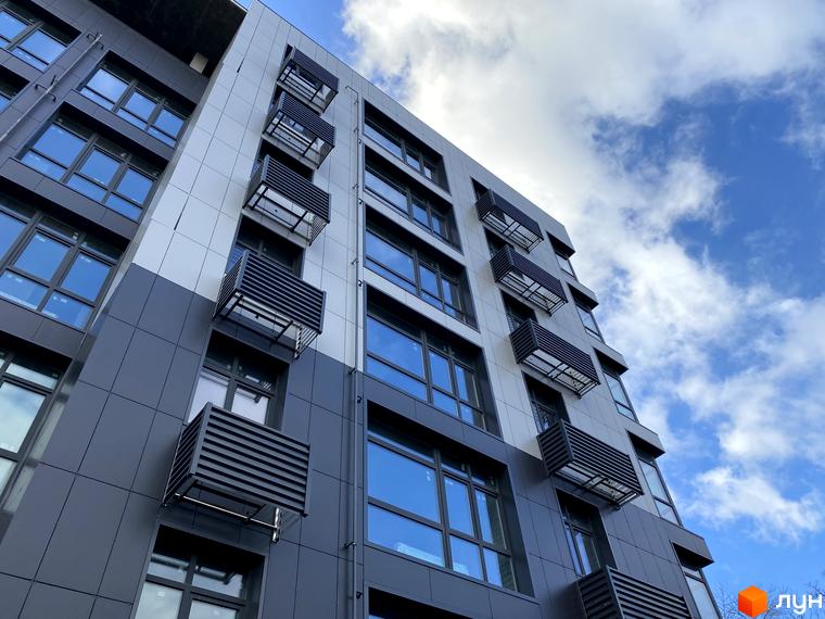 Фасад житлового комплексу Forest Hill з касетними балконами та великими вікнами на тлі блакитного неба з хмарами.