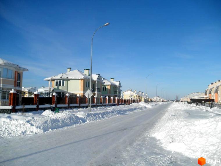 Зимовий пейзаж котеджного містечка Нова Богданівка. Будинки з двосхилими дахами, огорожі з цегли та кованого металу, засніжена дорога.