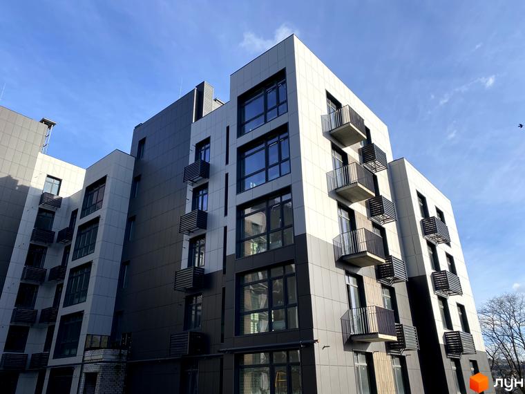 Фасад житлового комплексу Forest Hill з сірими та білими панелями, великими вікнами та балконами. Будинок розташований на фоні блакитного неба.