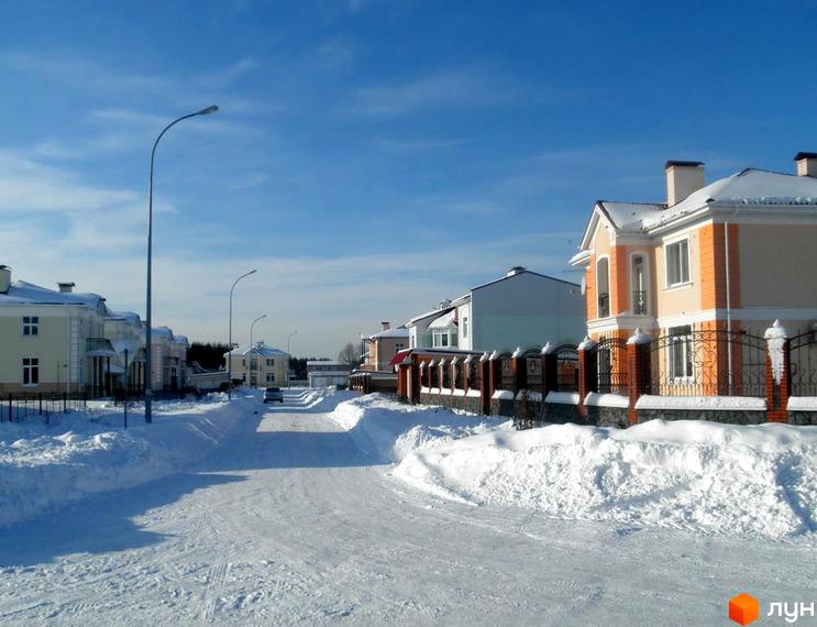 Зимовий пейзаж Котеджного містечка Нова Богданівка з будинками з білими стінами та снігом на вулицях. На передньому плані дорога, вкрита снігом.