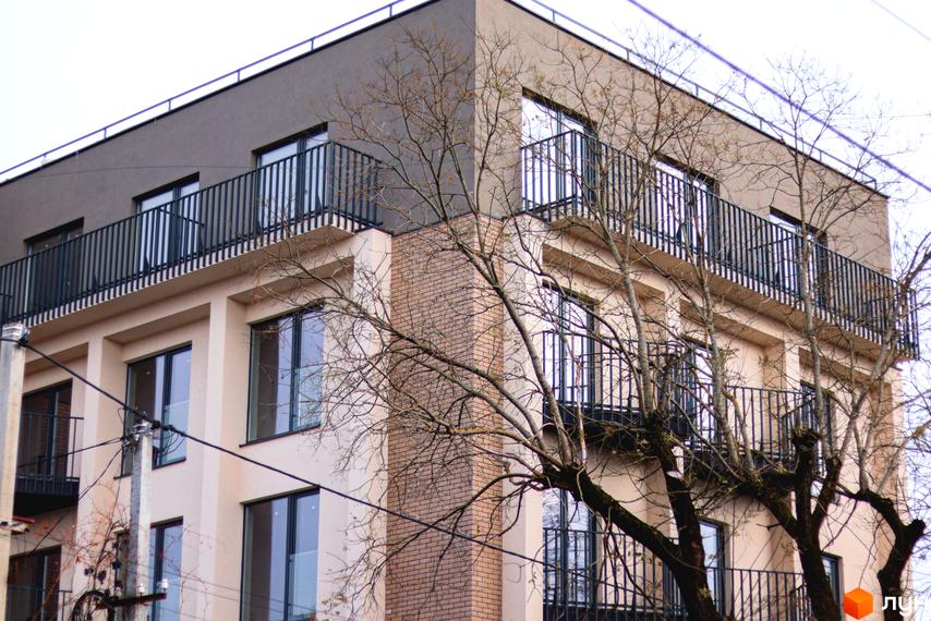 Фасад житлового комплексу Родовід з балконами та вікнами. Навколо будівлі ростуть дерева без листя.