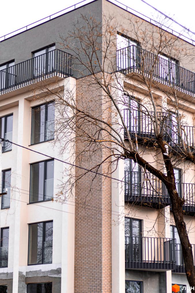 Зовнішній вигляд новобудови ЖК Родовід з балконами та вікнами. Навколо будівлі видно дерева без листя.