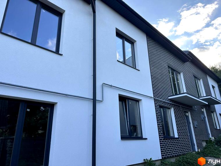 Житловий комплекс на вул. Стадникової, 41 з білим та темно-сірим цегляним оздобленням, вікнами та балконами. Прибудинкова територія має зелені насадження.