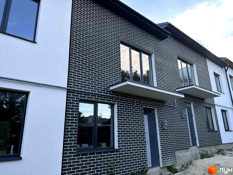 Фасад новобудови на вул. Стадникової, 41 з комбінованим оздобленням: чорна цегла та біла штукатурка. Видно вікна, двері та ґрунтову прибудинкову територію.