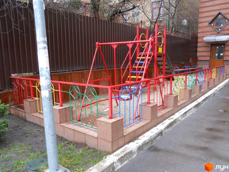 Дитячий майданчик з гойдалкою та гіркою біля цегляної новобудови на вул. Коперника, 11. Огороджена територія з різнокольоровою огорожею та покриттям.