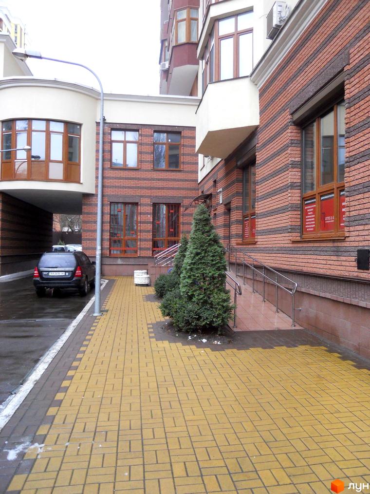 Житловий комплекс на вул. Коперника, 11. Фасад будинку з цегли та білої штукатурки, поруч доріжка з жовтої плитки та зелені насадження.