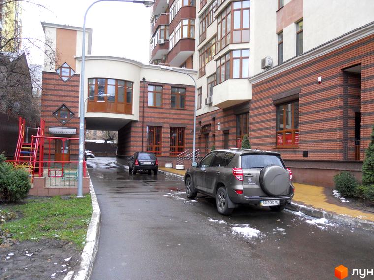 Житловий комплекс на вул. Коперника, 11. Зовнішній вигляд будівлі з цегляним оздобленням та прибудинкова територія з автомобілями та дитячим майданчиком.