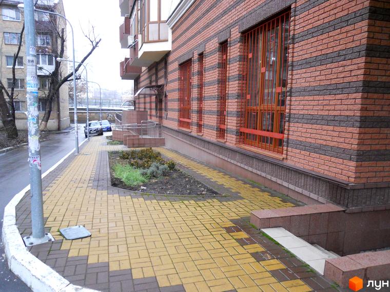 Фасад житлового комплексу вул. Коперника, 11, з цегляним оздобленням та великими вікнами. Поруч розташована брукована алея та зелена зона.