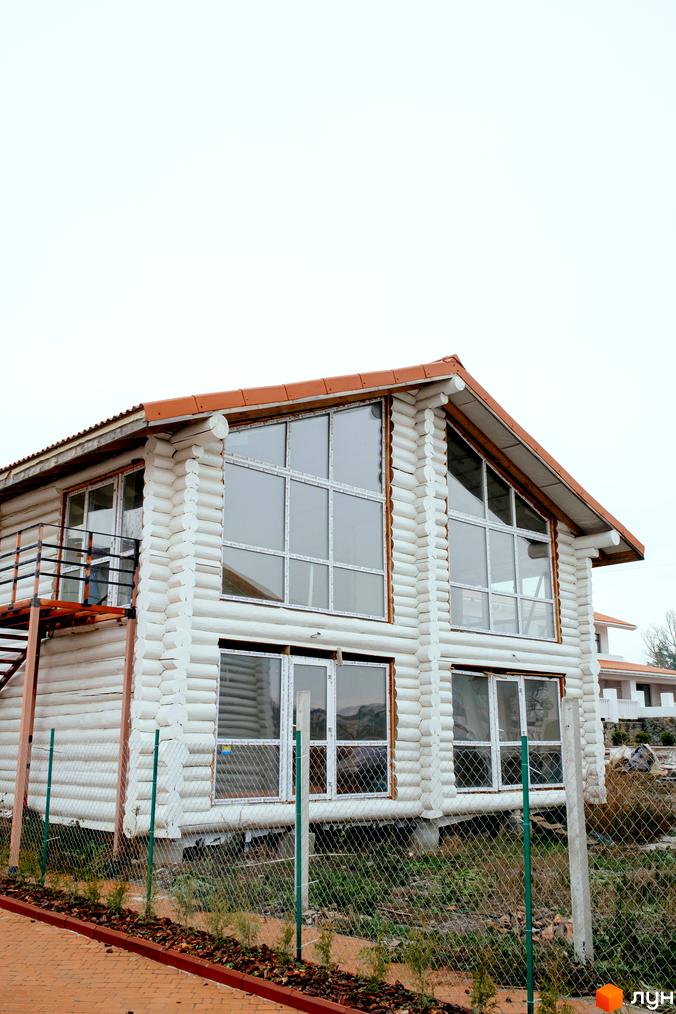 Зовнішній вигляд двоповерхового будинку з білих дерев'яних колод та великими вікнами. Навколо будинку огороджена територія з парканом та доріжкою.