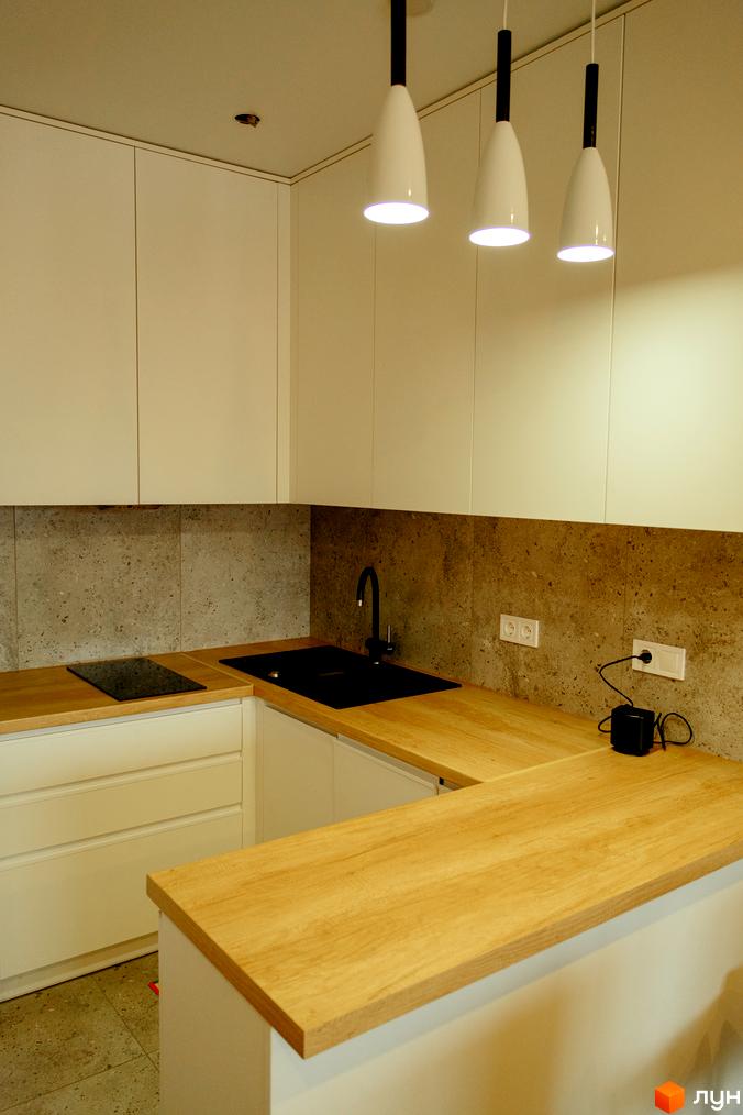 Кухня в стилі мінімалізм з білими фасадами, дерев'яною стільницею та сірим фартухом. Індукційна плита та чорна мийка з змішувачем.