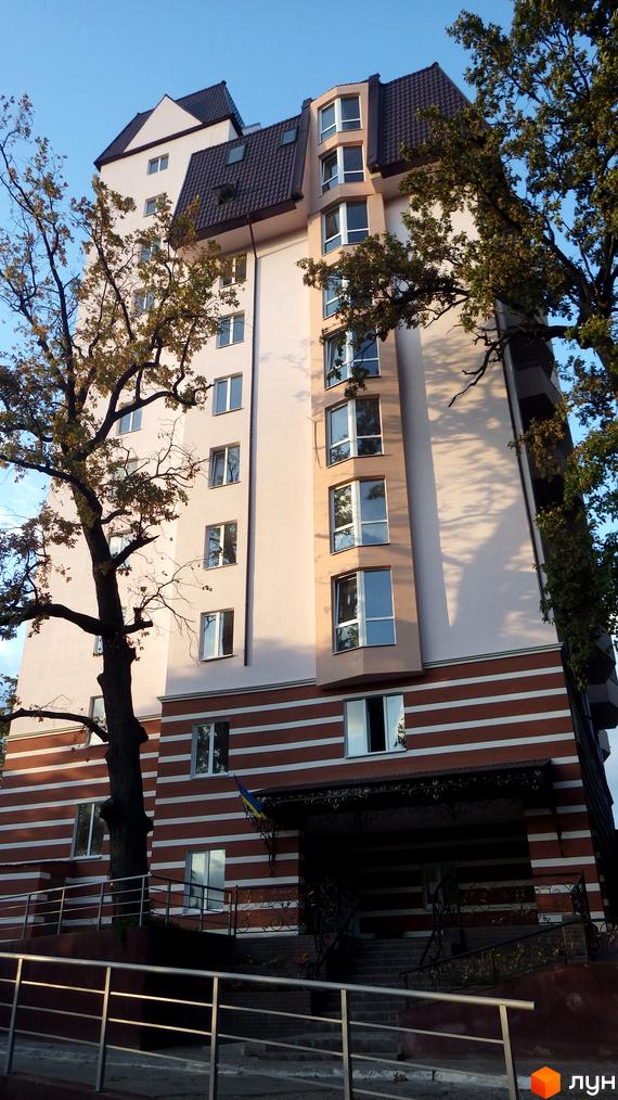 Висотна будівля з великими вікнами та коричневим дахом. На фасаді будівлі чергуються смуги білого та коричневого кольору, а також присутні дерева.
