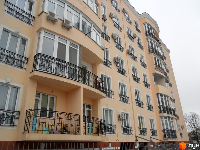 Зовнішній вигляд фасаду житлового комплексу Посольський, з балконами та кондиціонерами. Навколо будинку видно огорожу та дерева.