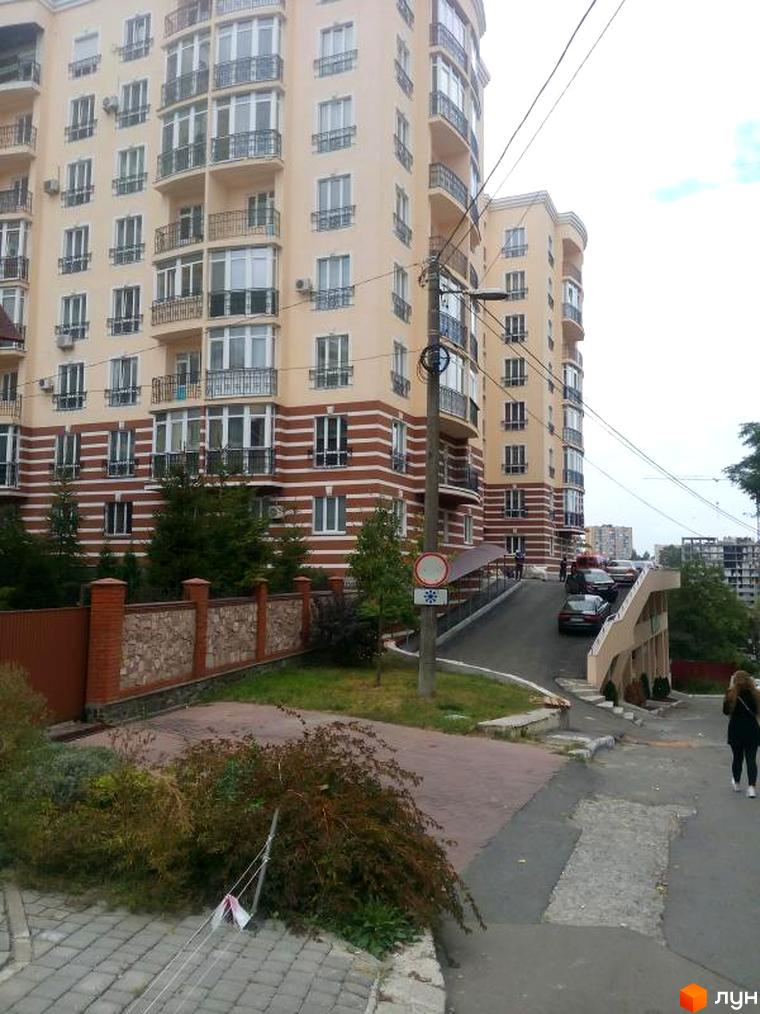 Зовнішній вигляд багатоповерхового будинку ЖК Посольський з балконами та вікнами. Прибудинкова територія з дорогою та зеленими насадженнями.