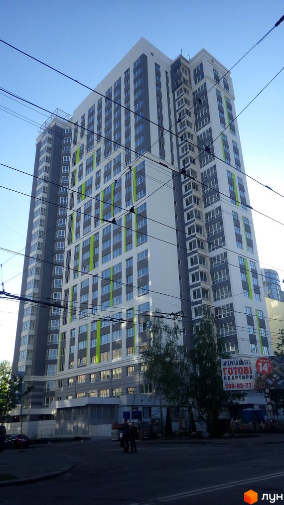 Новобудова ЖК Лук'янівський з сірими та білими фасадами та зеленими акцентами. Зовнішній вигляд будинку з багатьма вікнами та балконами.
