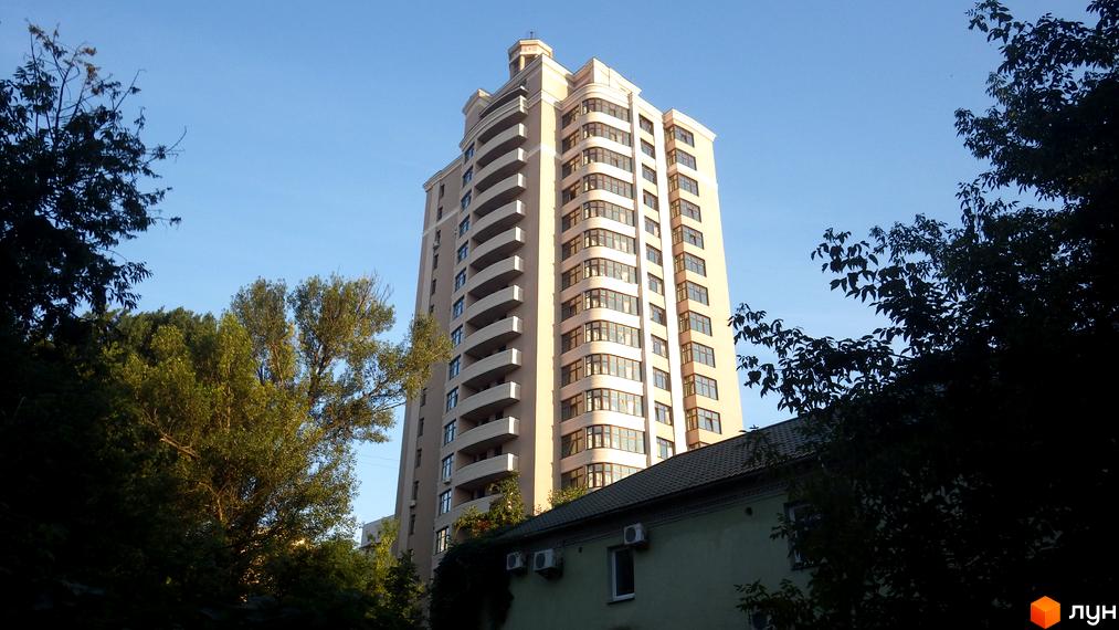Житловий комплекс Столичний Дім – висока світла новобудова з численними балконами та вікнами, оточена деревами та зеленню.