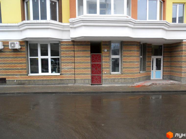 Фасад Житлового комплексу на вул. Коперника, 7 з жовтим верхнім поверхом та смугастою цегляною кладкою. Перед будинком мокра дорога.