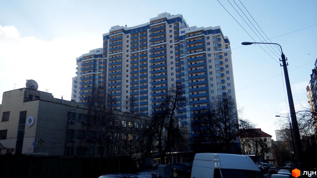 Зображення Житлового комплексу Старокиївський. Висотна будівля з балконами та блакитним оздобленням. На передньому плані дерева та інші будівлі.