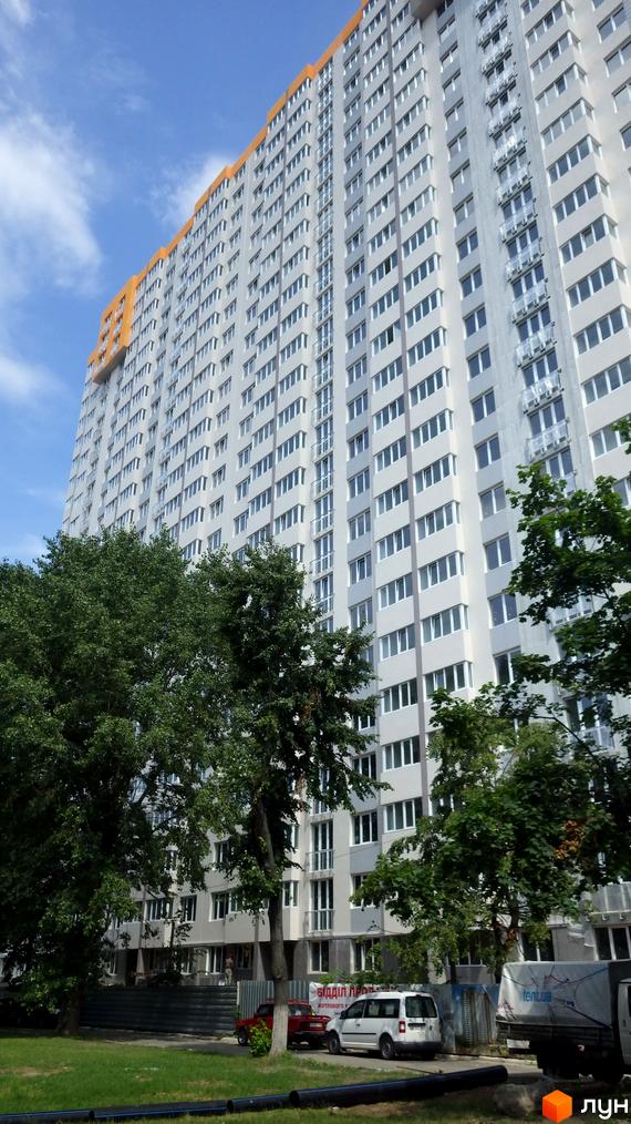 Фото багатоповерхового будинку в Житловому комплексі Лідер. Вид на фасад будівлі та прибудинкову територію з деревами.