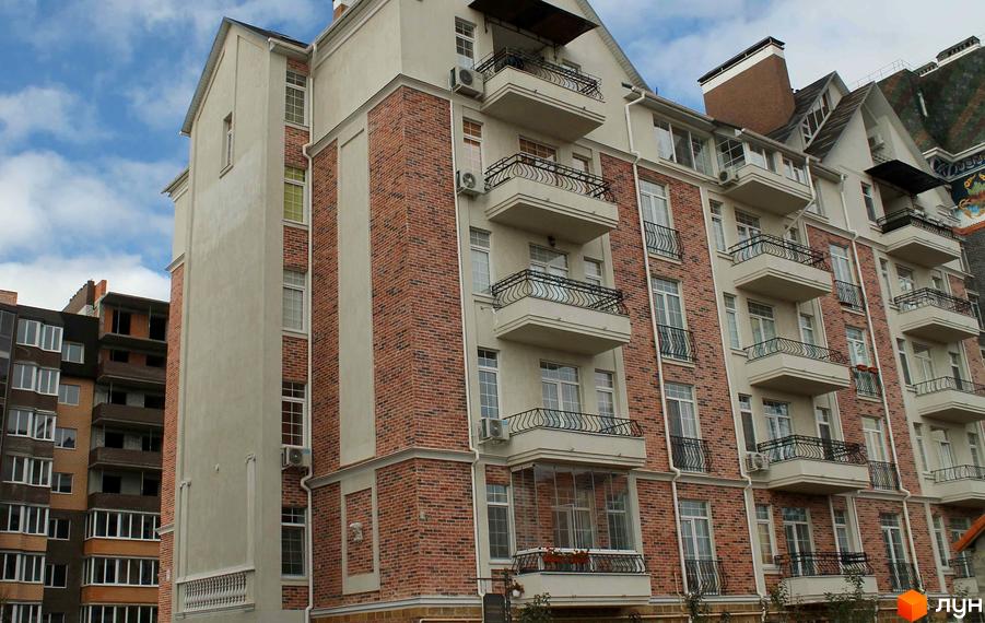 Фасад житлового комплексу English House в місті Зелений Мис. Будинок з цегляною обробкою та балконами, на тлі хмарного неба.