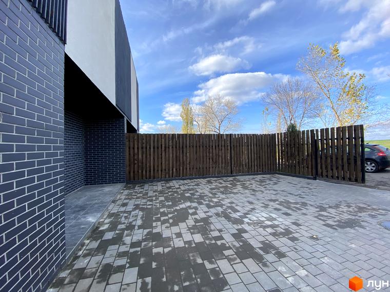 Таунхаус Новоолександрівський: сіра цегляна стіна та дерев'яний паркан на прибудинковій території з бруківкою.