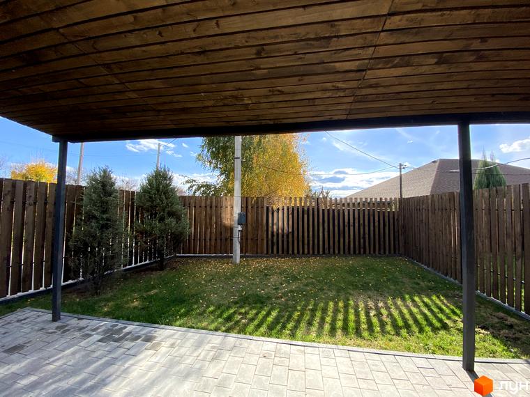 Таунхаус „Новоолександрівський“: вид з тераси на зелений двір з парканом та деревами. Сонячний день, блакитне небо з хмарами.