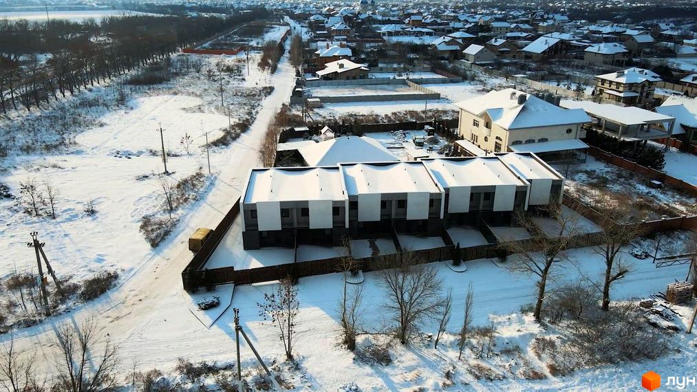 Таунхаус „Новоолександрівський“ взимку. Три сучасні двоповерхові будинки з біло-сірими фасадами та пласкими дахами, розташовані на засніженій ділянці з парканом та деревами.