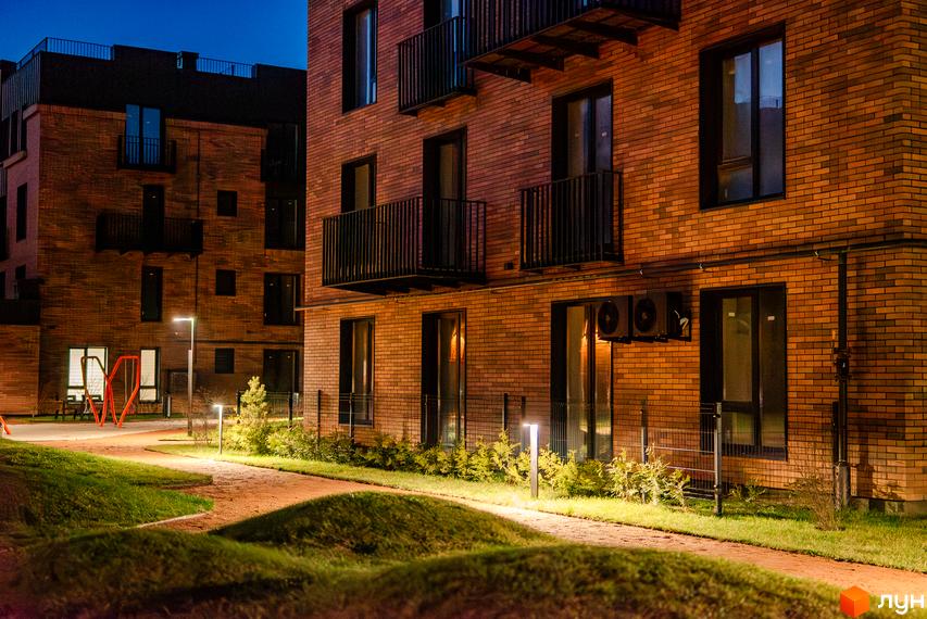 Житловий комплекс Клубне містечко 12 з цегляним фасадом та балконами, освітлена доріжка та зелена прибудинкова територія ввечері.