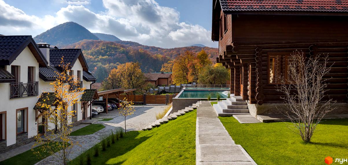 Будинки Apartel Shayan Villas: білі котеджі з темними дахами та дерев'яний будинок з червоним дахом. Прибудинкова територія має басейн, газони та парковку на тлі осінніх гір.