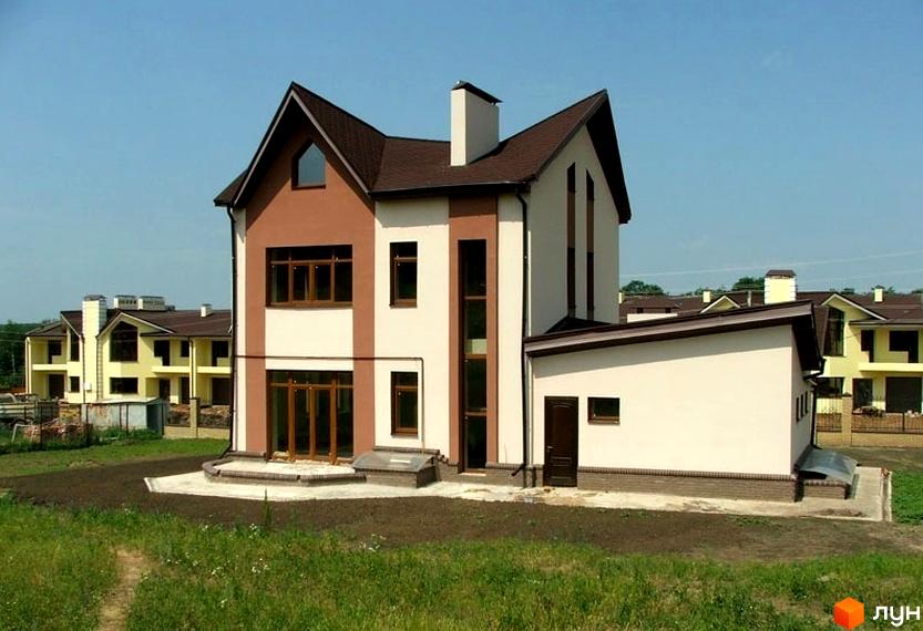 Двоповерховий будинок з коричневим дахом та оздобленням фасаду. Навколо будинку зелена трава та інші будинки на задньому плані.