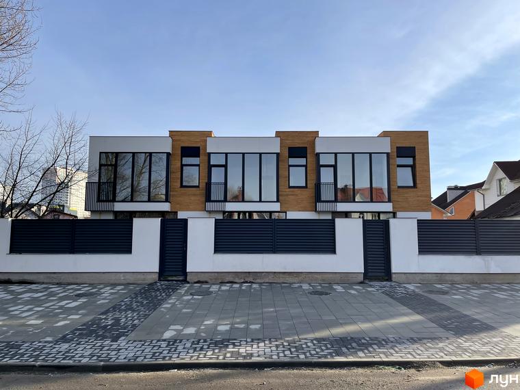 Таунхауси Gatne Country Club - двоповерхові будинки з великими вікнами та дерев'яними елементами фасаду, огороджені парканом з воротами. Перед будинками розташована вимощена плиткою територія.