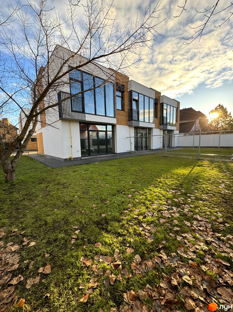 Зображення таунхаусів Gatne Country Club з великими вікнами та балконами. Навколо будинку зелений газон з опалим листям.